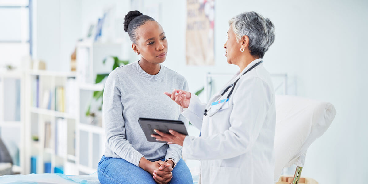 A woman consults with a doctor while seated on a bed in a medical setting, discussing her health concerns.