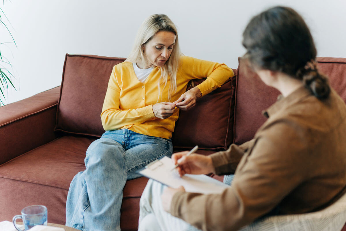 A therapy session with a woman sitting on a couch, speaking to a counselor taking notes.